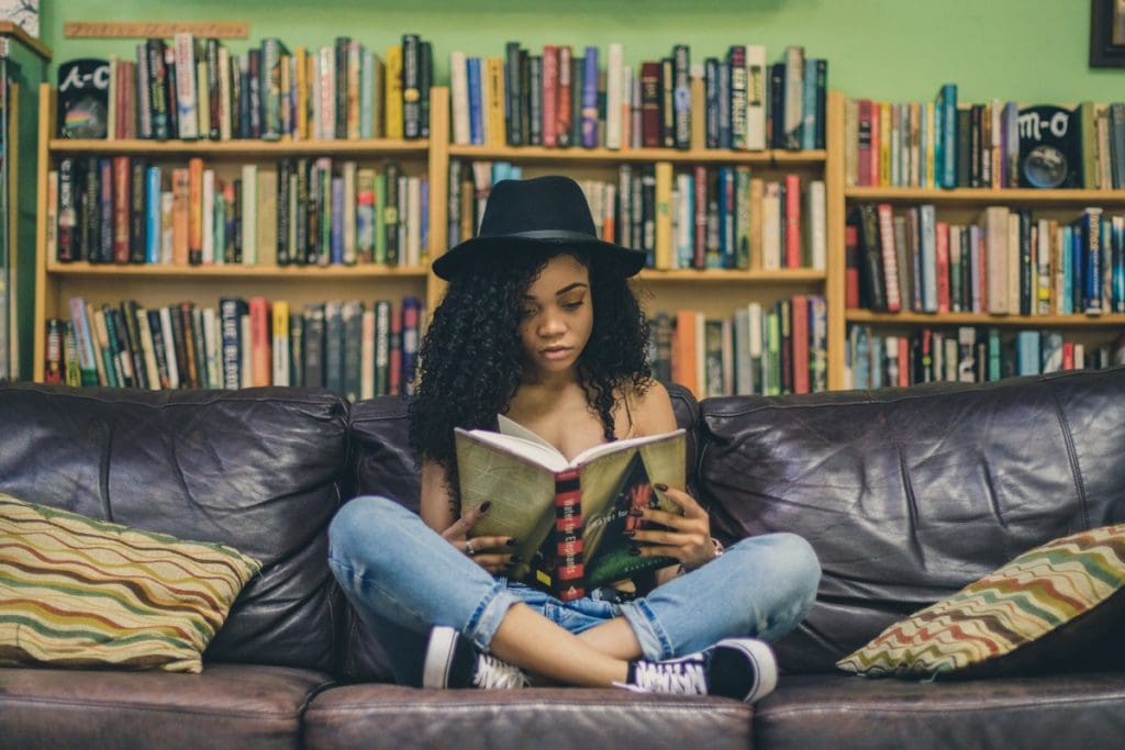 A teen girl reads a book in the middle of a bookstore, books are a great way to keep kids entertained while traveling.