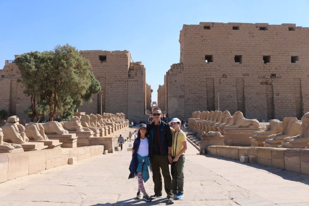 Two kids and their dad stand together in front of ancient buildings of the Temple of Karnak near Luxor, a must on this 2-Week Egypt Itinerary for Families.