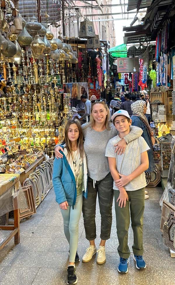 A mom and her two kids stand in an Egyptian market filled with things to buy.