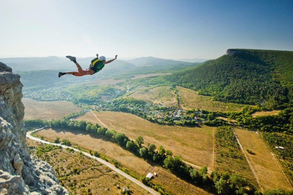 A teen girl base jumps from a cliff.