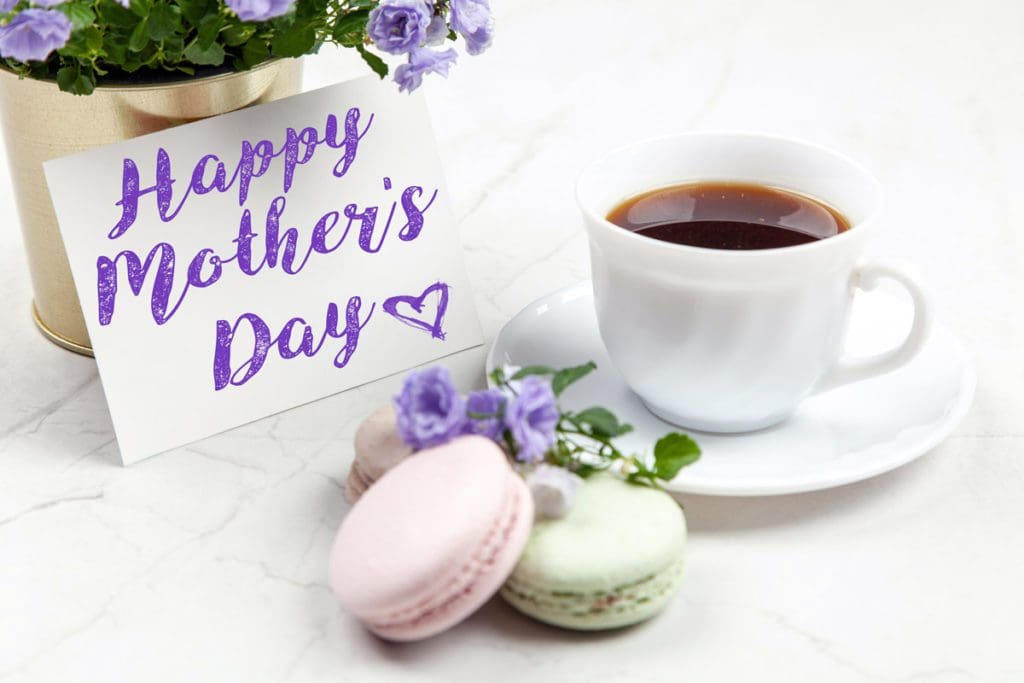 A card that reads "Happy Mother's Day" next to a cup of tea and pastel-colored macrons.