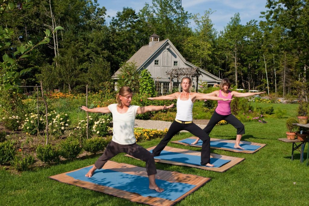Three women do outdoor yoga near the garden at Hidden Pond.