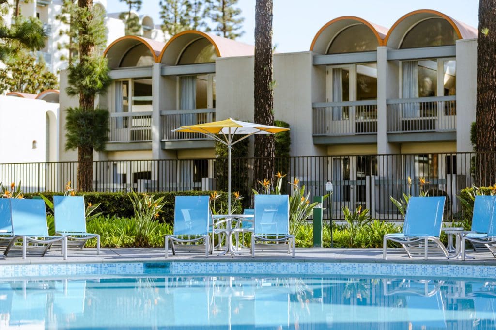 The beautiful garden pool, with surrounding pool deck featuring blue chairs and garden features, at Howard Johnson Anaheim.