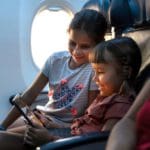 Two kids play a game on an iPad together on an airplane.