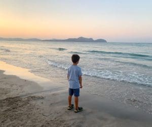 A young boy looks out onto the ocean near Mallorca at sunset.