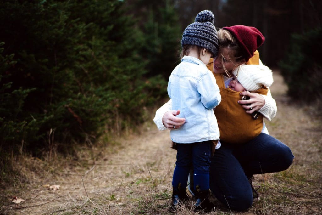 A mom hugs her two children while traveling along a hiking trail together.