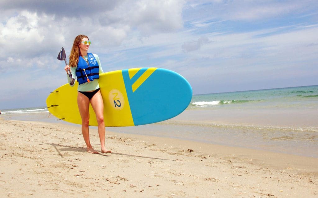 A woman walks across the sand with a paddleboard at Delray Beach.