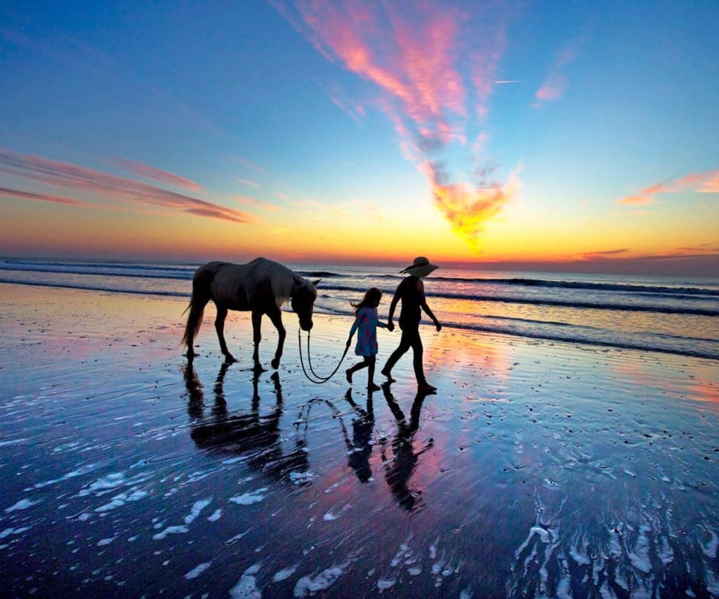 Mother and daughter walking a horse on the beach at sunset on Amelia Island, one of the best places to stop on an NYC to Miami itinerary for families!