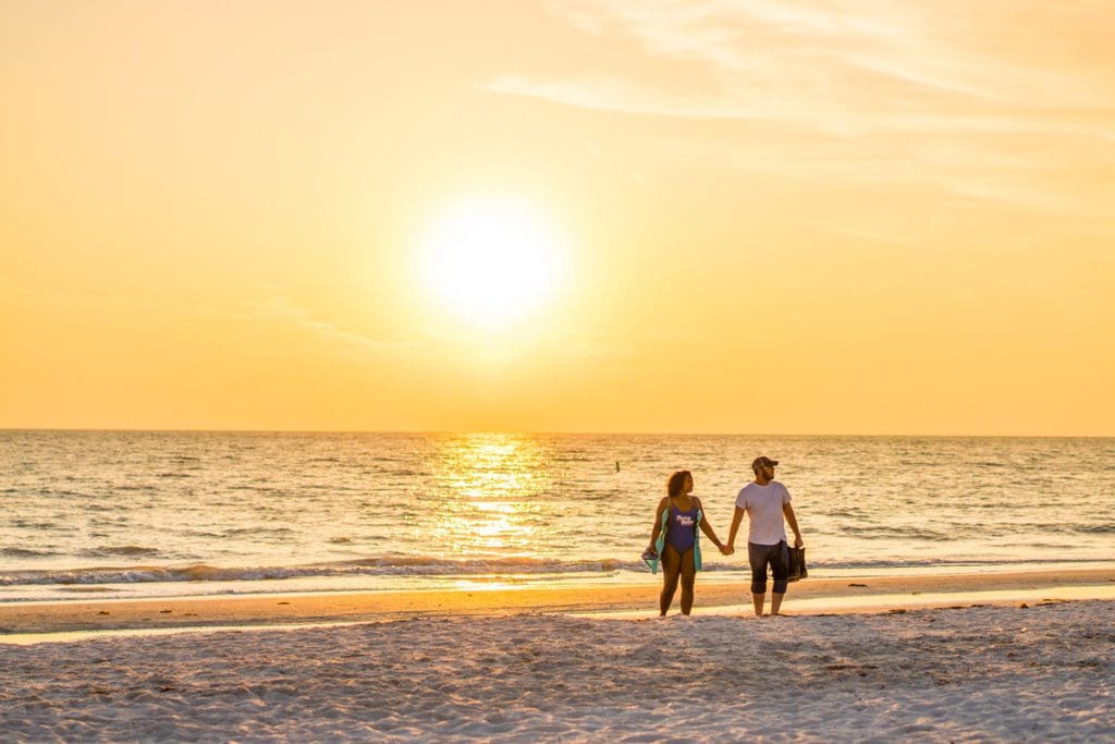 A couple walks hand-in-hand along the St. Pete Beach at sunset, one of the best Florida beaches for families.