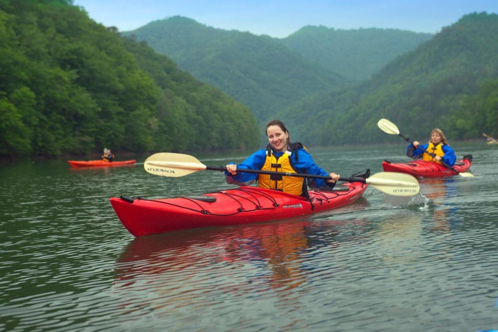 Two people, in their own kayaks, paddle across Fontana Lake with mountains in the distance.