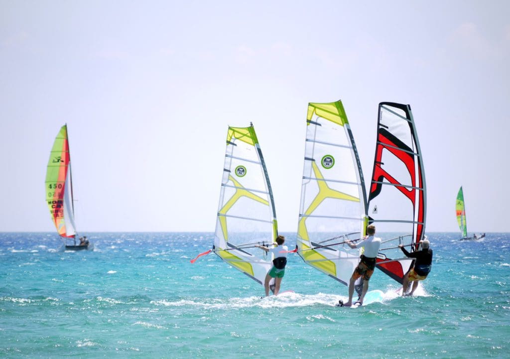 Two teen boys and their dad windsurf in the ocean on a sunny day.