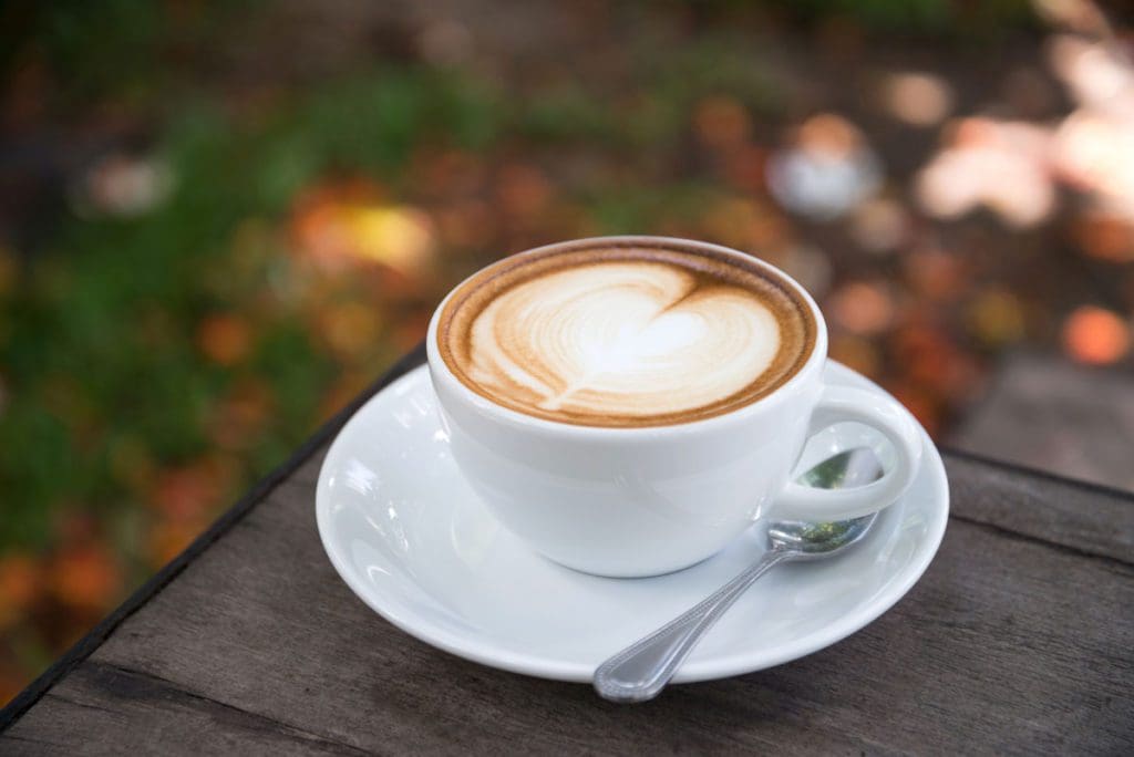 A latte with a heart design in the foam on a corner of a table.