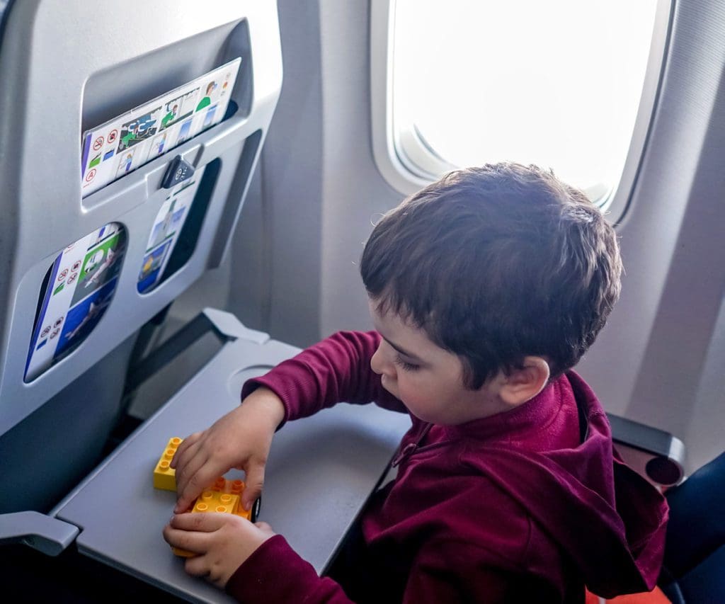 A young boy plays with legos on his airplane tray table during a flight. If you're wondering about Allegiant Airlines policies for kids, onboard entertainment is usually sparse. 