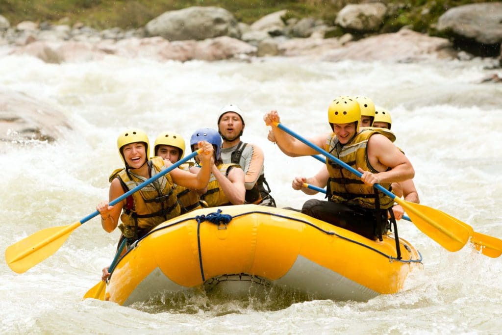 A family white water rafts down a raging river, one of the best extreme sports to do with teens on a family trip.