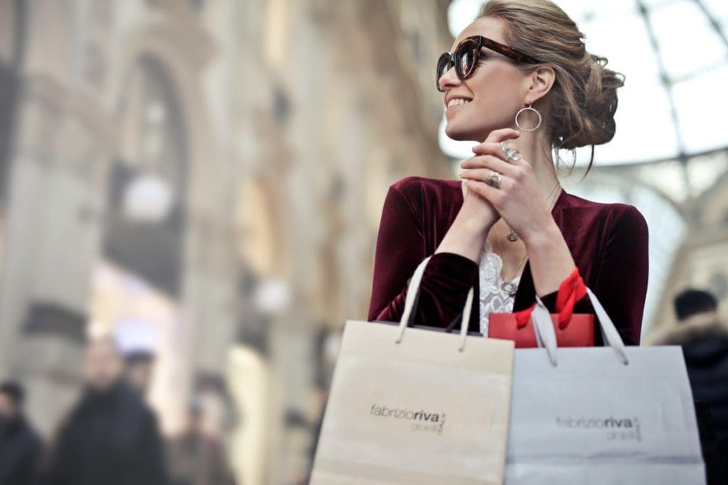 A mom smiles while she walks around with two shopping bags.