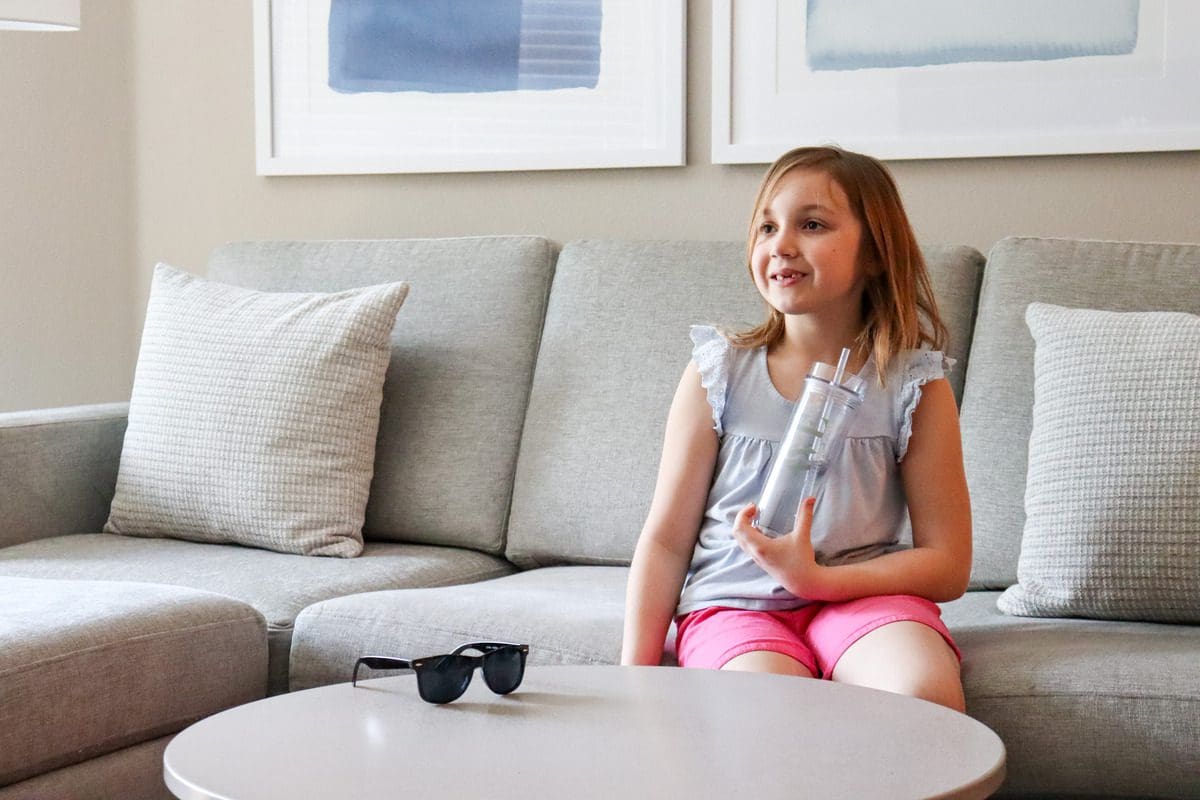 A young girl sits on a couch within a furnished apartment at AVE Tampa Riverwalk.