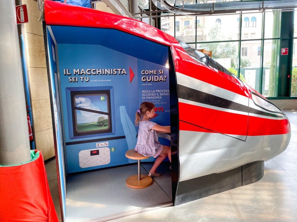 A young girl pretends to drive an Italian train, while visiting Explora il Museo dei Bambini di Roma.