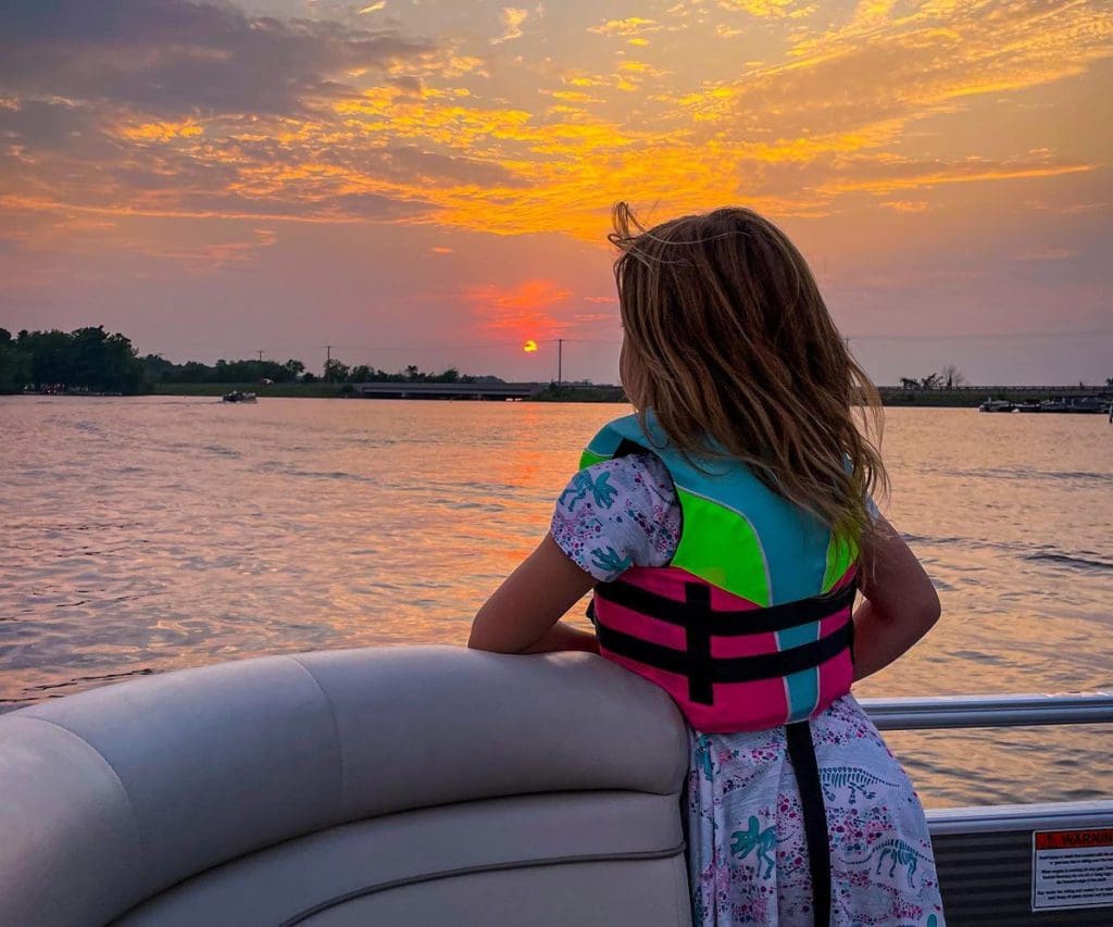A young girl watches a sunset from a pontoon on Lake Wissota, one of the best places to rent a lake house in Wisconsin.
