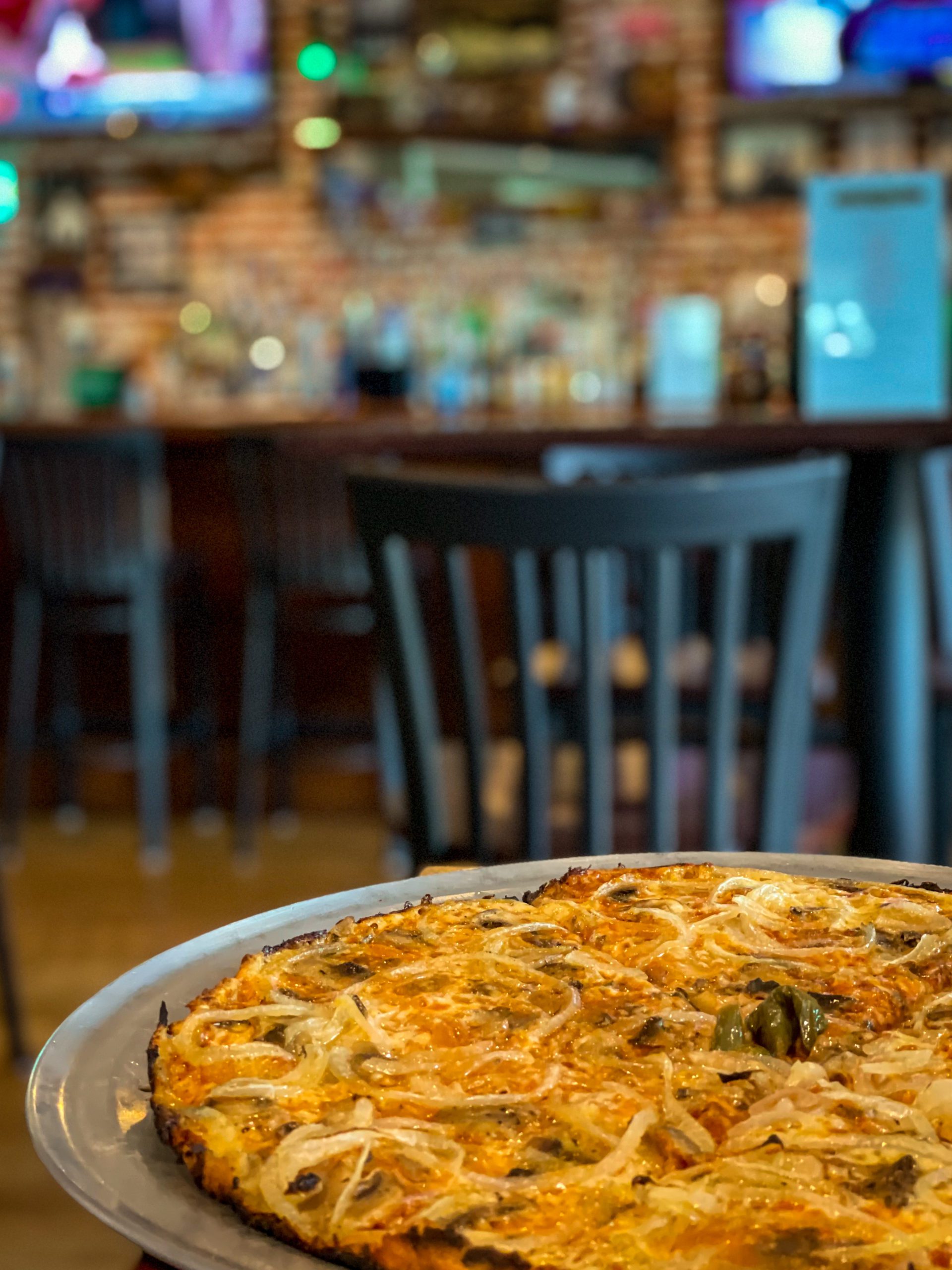 A pizza at Colony Grill in Midtown Tampa, with the bar in the background, a must eat when you visit Tampa Bay with Kids.