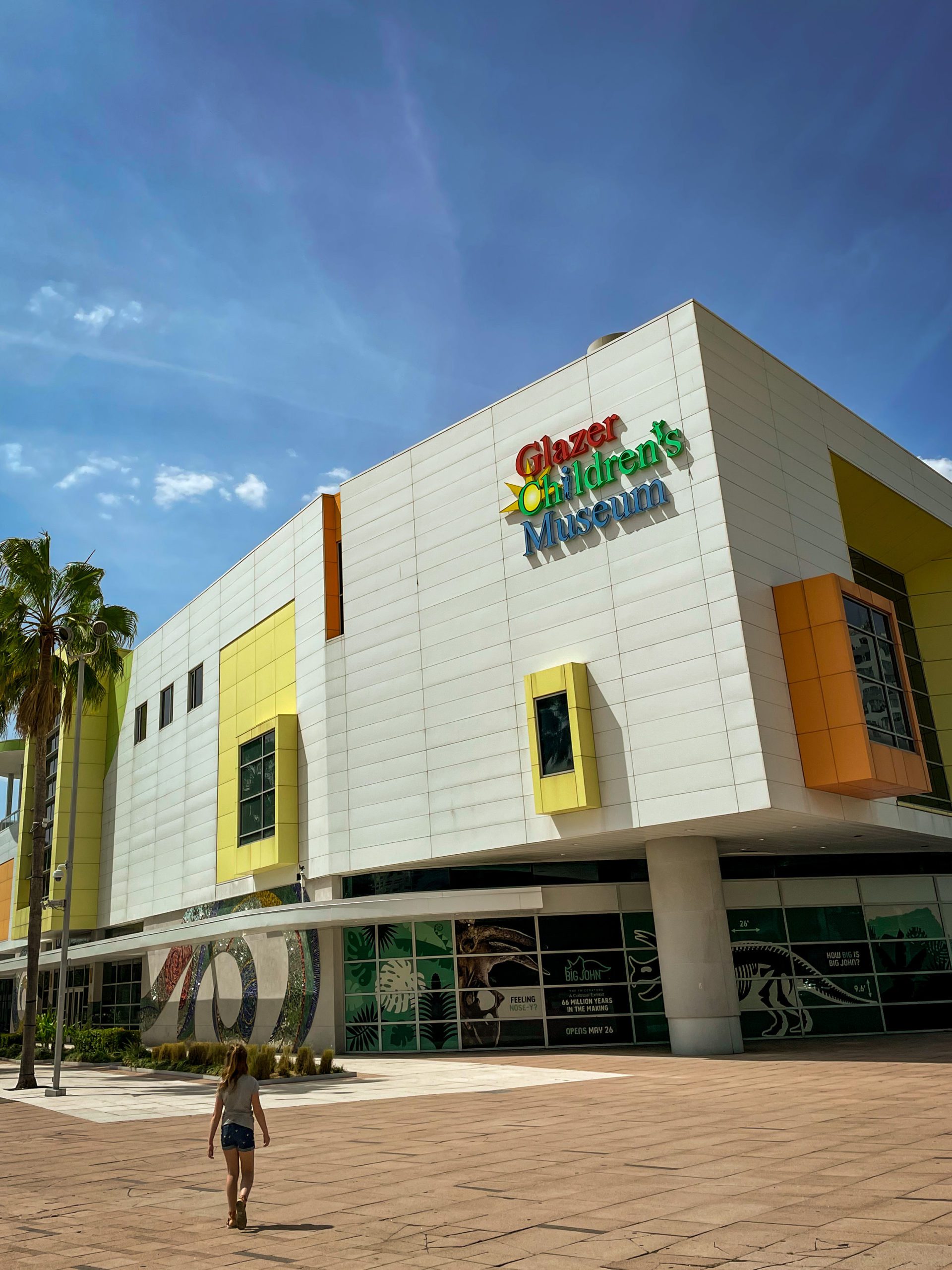 A young girl walks toward the door of Glazer Children's Museum on a sunny day.