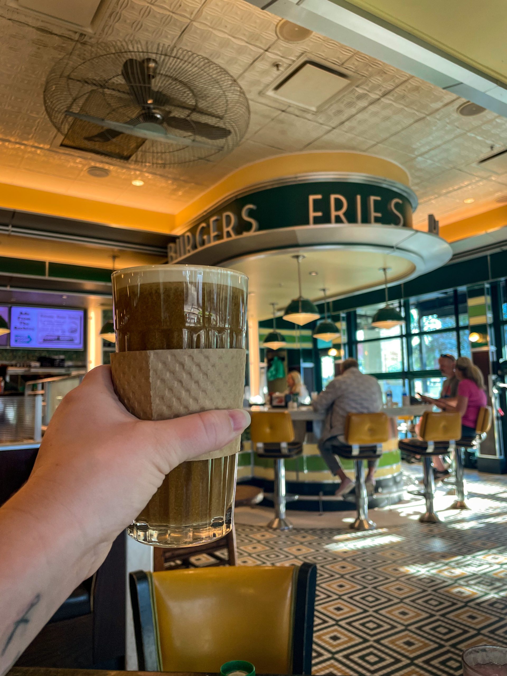 A woman holds up a Cuban coffee, while dining at Goody Goody Burgers.