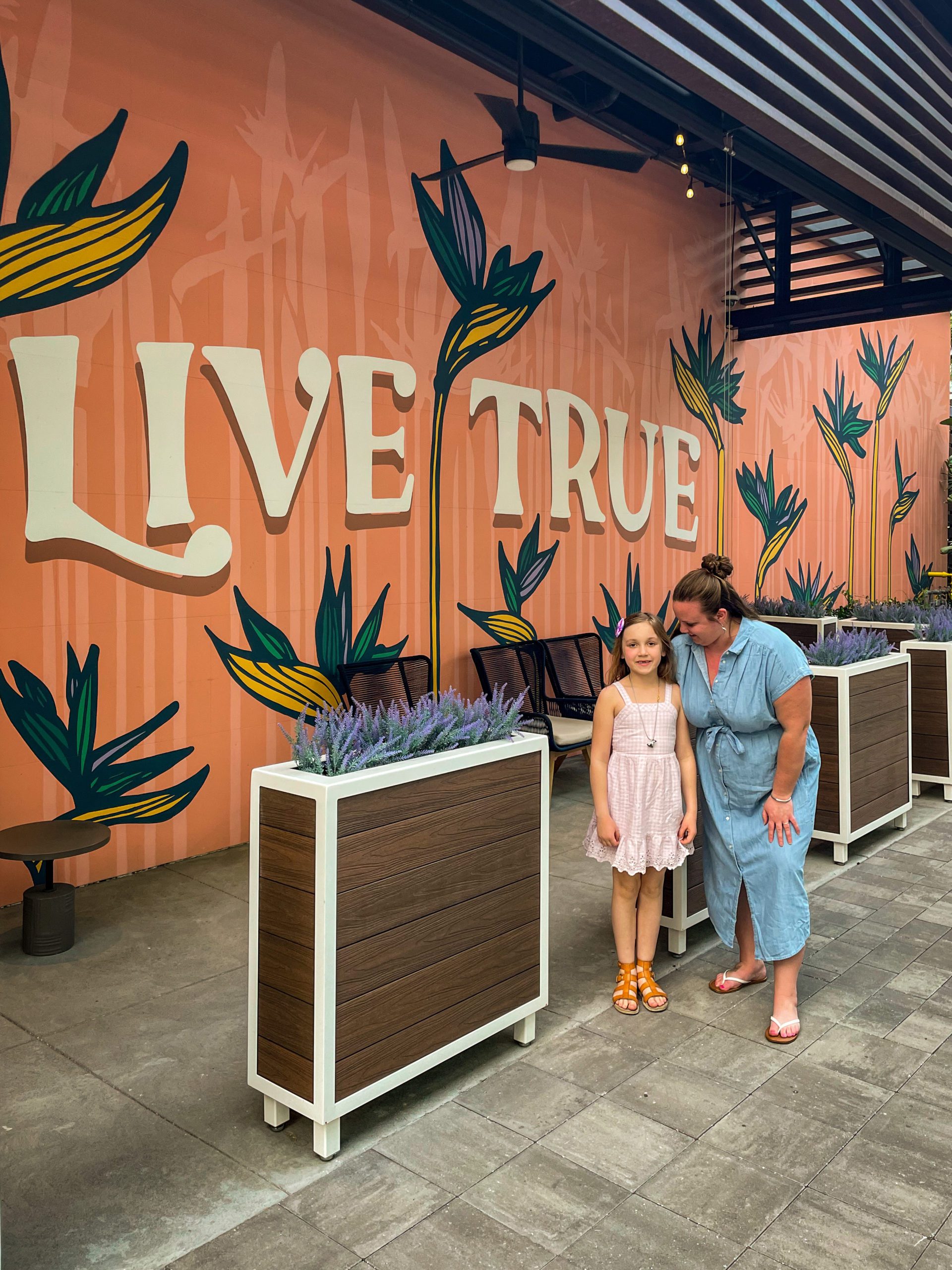 A young girl and her mom stand in front of a mural that says "Live True" in Midtown Tampa.