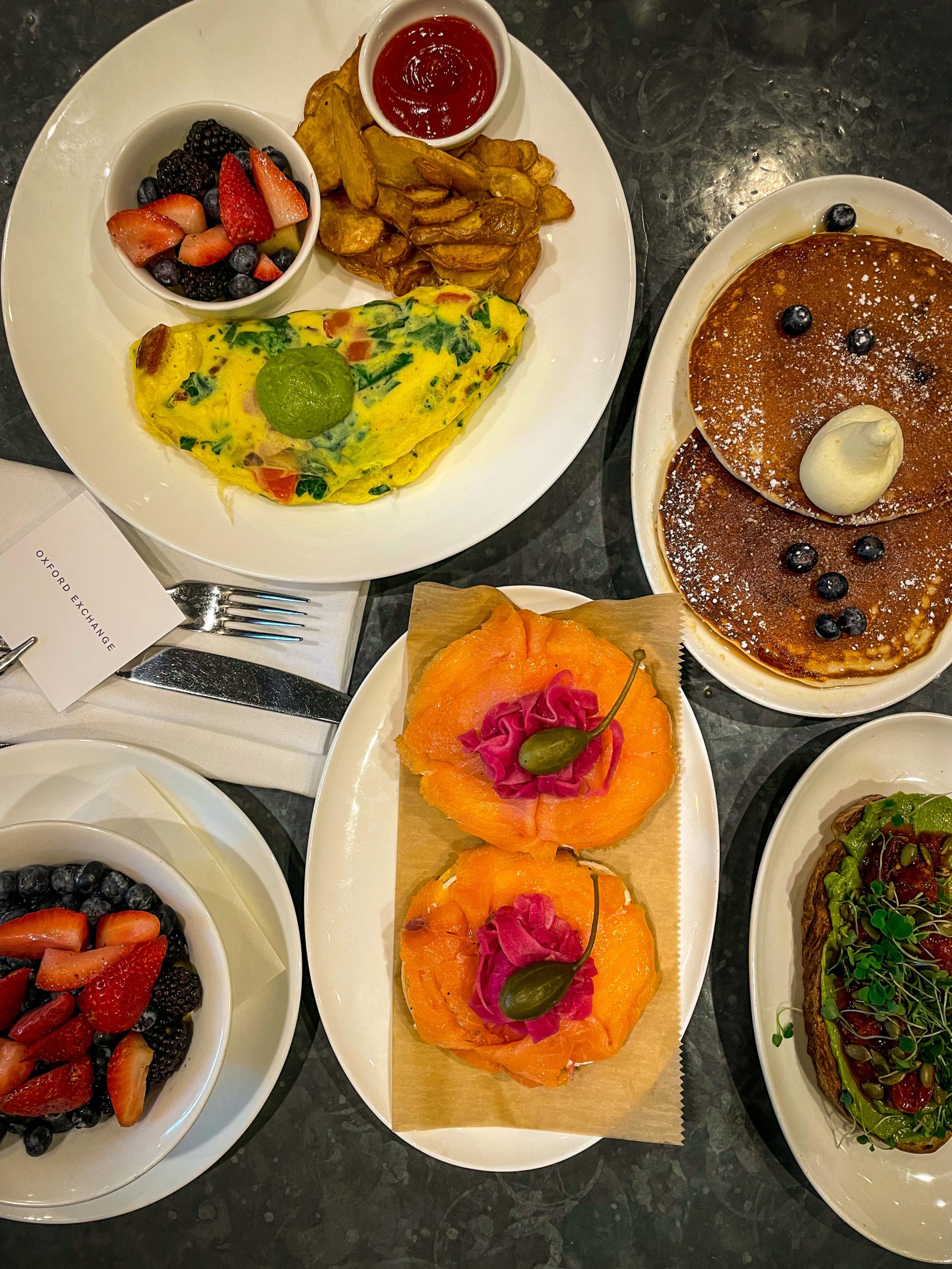 A table spread of breakfast food items, including pancakes and an omelette, at Oxford Exchange.