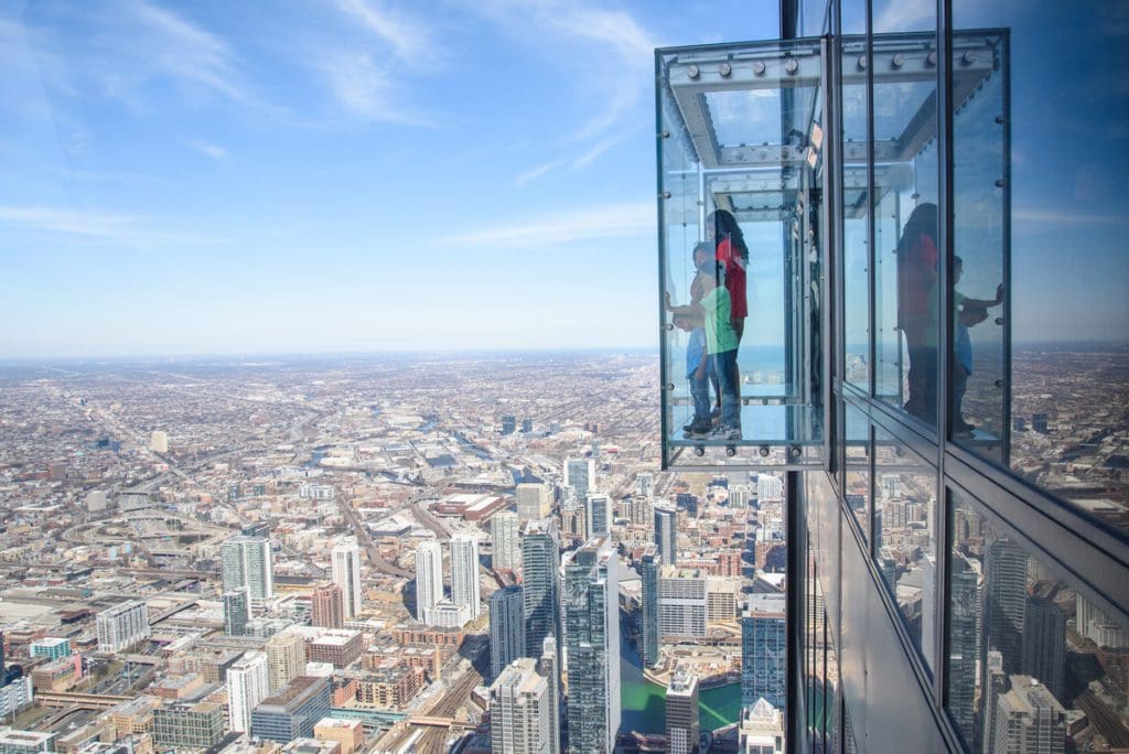 People stand in a glass observation area at the Chicago Skydeck looking out onto the city below.