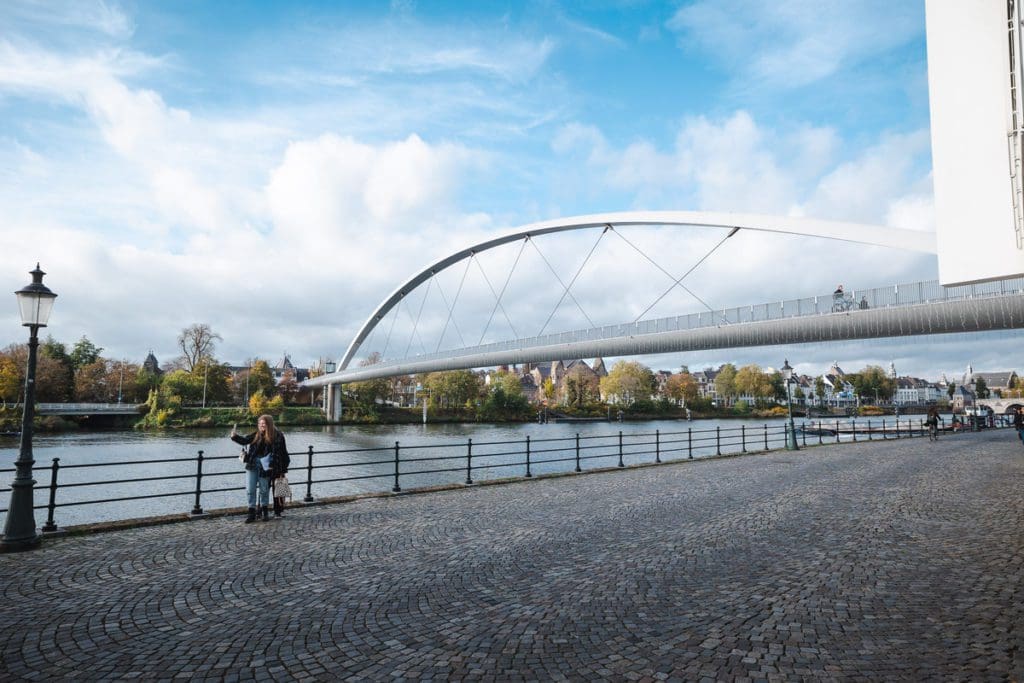Pedestrians taking a selfie with a bicycle bridge over a canal in the background in Maastricht, one of the best places to visit in the Netherlands with kids.