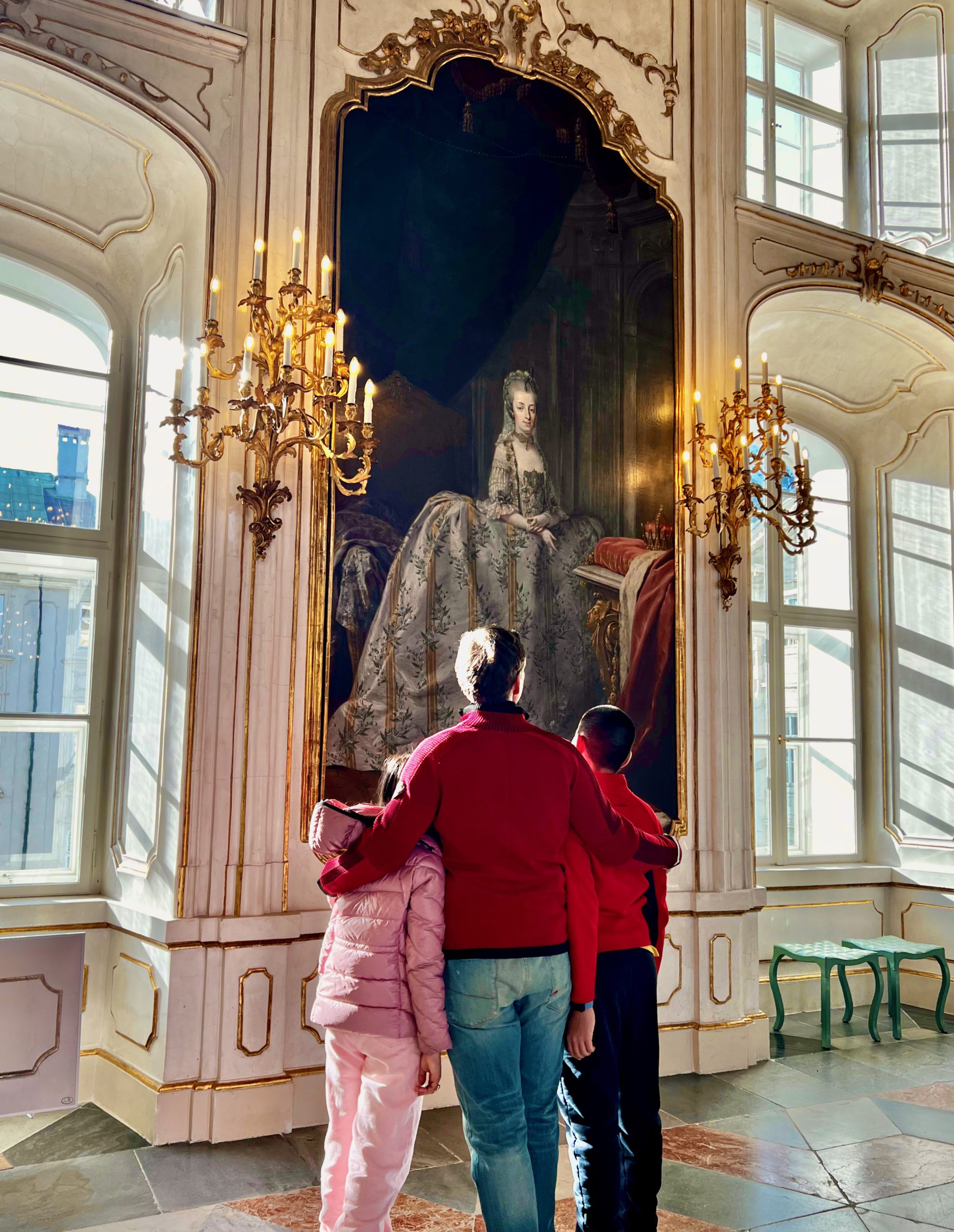 A dad and his two kids enjoy a large painting of a long-ago royal at the Imperial Palace, one of the best things to do in Innsbruck with kids this winter.