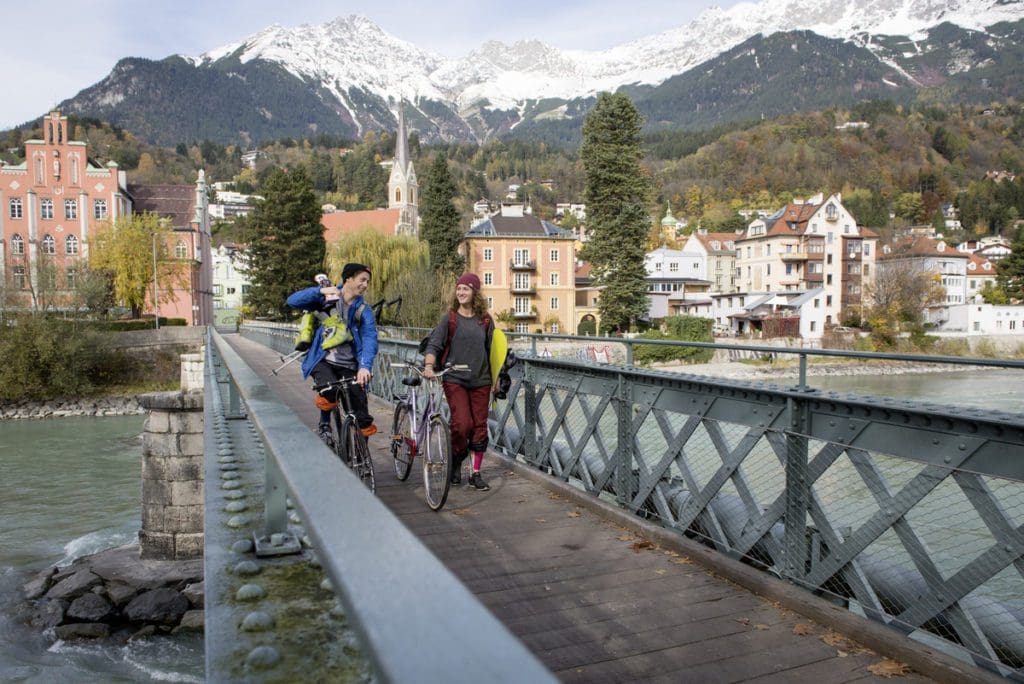People walk across a bridge in Innsbruck with their ski gear, skiing is one of the best things to do in Innsbruck with kids this winter.