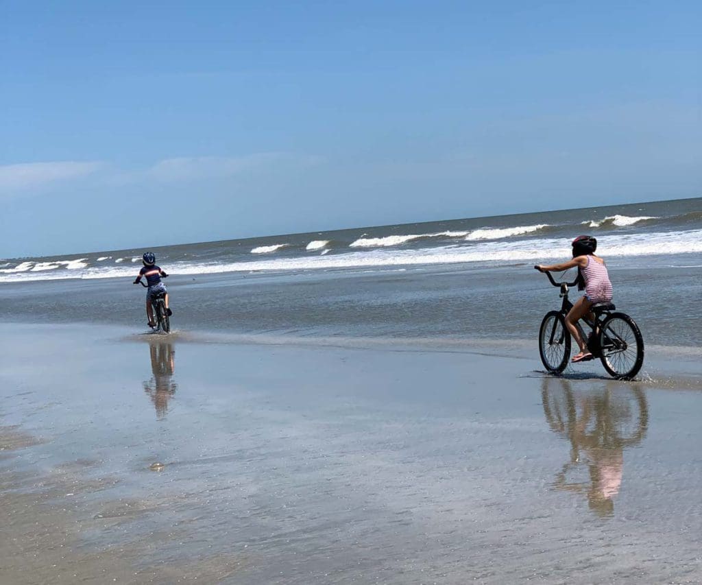 Two young kids riding bikes on a beach on Kiawah Island, one of the best beaches in South Carolina for families. 