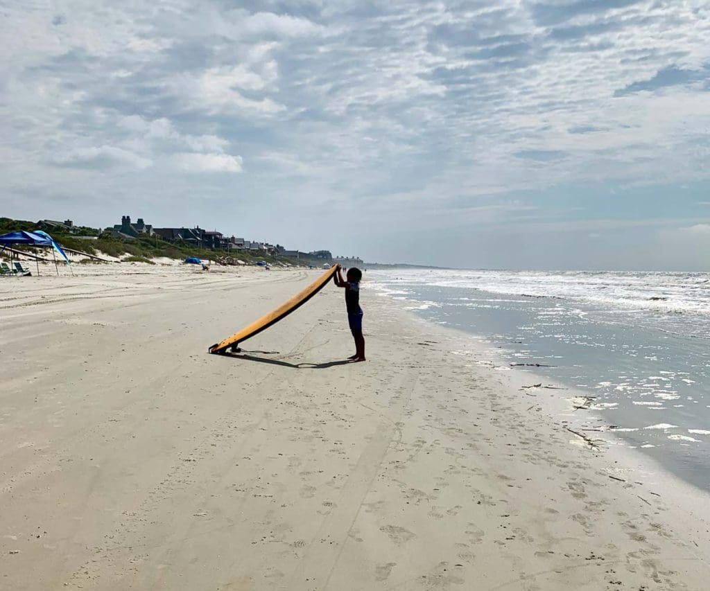 A young girl standing on a beach holding a surfboard on Kiawah Island.