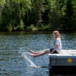 A young girl sits at the end of a dock and kicks at the lake, while visiting one of the best Minnesota lakes with her family.