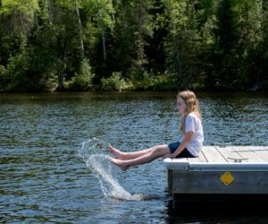 A young girl sits at the end of a dock and kicks at the lake, while visiting one of the best Minnesota lakes with her family.