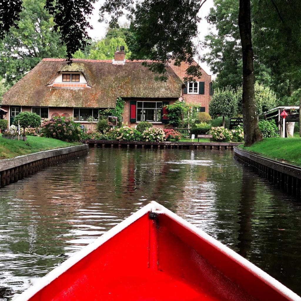 The nose of a small boat points toward a lovely cottage along the side of a canal in Giethoorn, one of the best places in the Netherlands with kids.