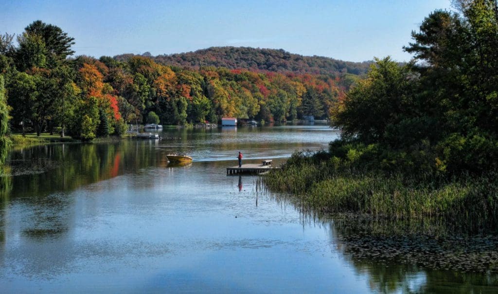 A man fishes from a dock on Lake Leelanau, one of the best lakes in Michigan for a family vacation, as a boat speeds by.