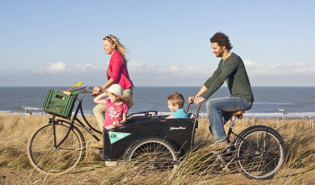 Young family is cycling in the dunes with the Northsea at the background, while visiting The Hague with kids.