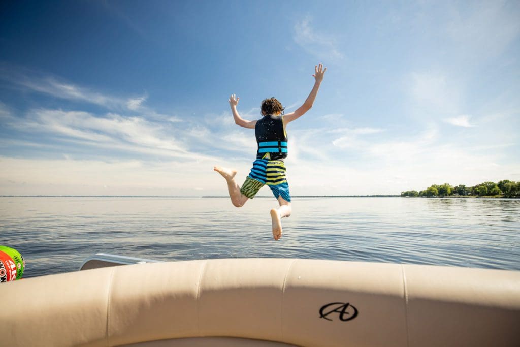 A young boy jumps from a pontoon into Lake Winnebago, one of the best places to rent a lake house in Wisconsin.