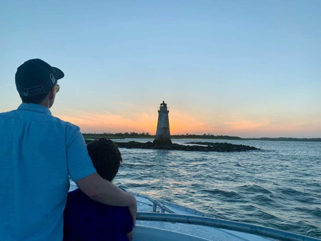 A man and a boy are on a beach looking at a lighthouse off the coast of Tybee Island, one of the best places to visit on a Savannah itinerary with kids.