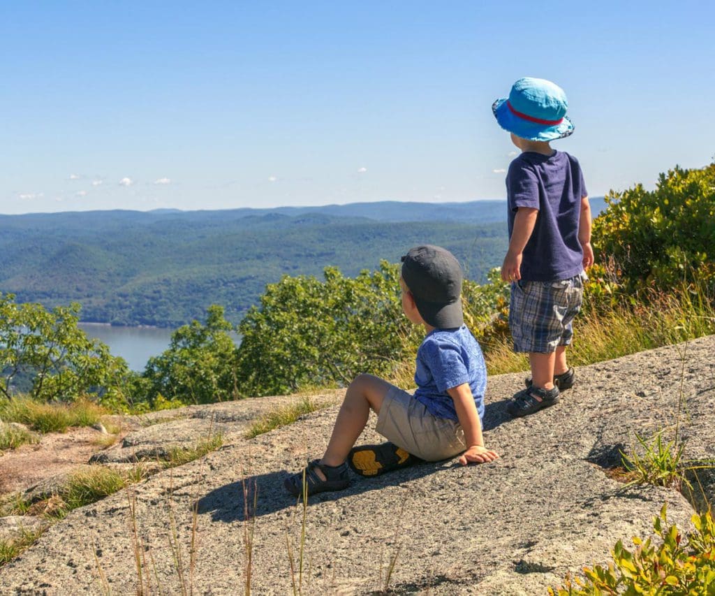 Two kids stand together looking out onto a scenic view from Bear Mountain, one of the best places to visit during Memorial Day Weekend near NYC for families.