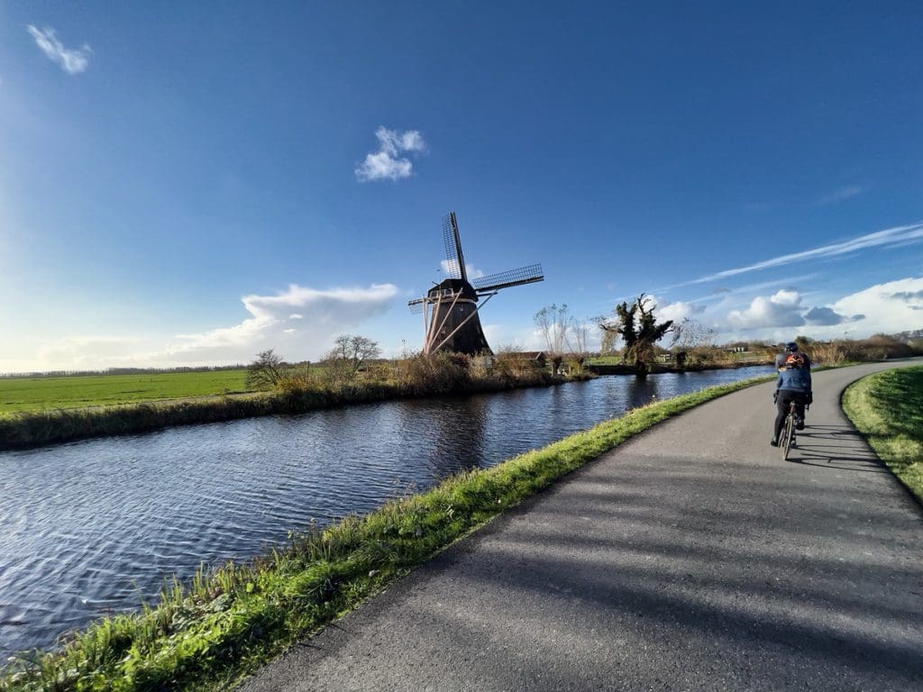 Two cyclists enjoy a sunny day on a bike path that passes Dutch windmills in Abcoude.