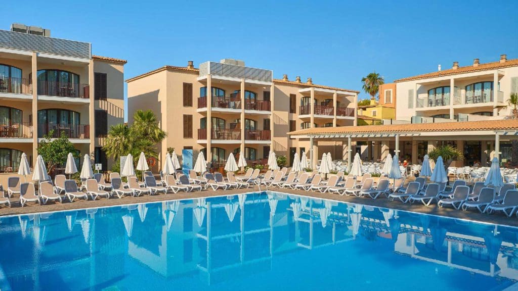 The pool with surrounding pool deck and loungers at Protur Floriana Resort Aparthotel, with resort buildings in the background.