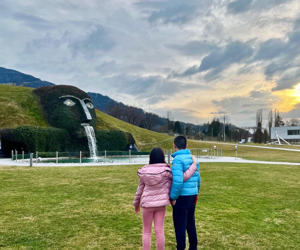 Two kids stand outside looking at the grass sculpture at the Swarovski Crystal World near Innsbruck.