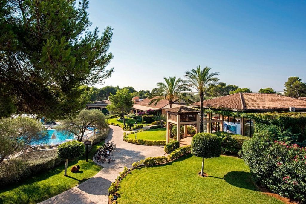 The lush grounds of Vell Mari Hotel and Resort, with a resort building and pool along a paved path.