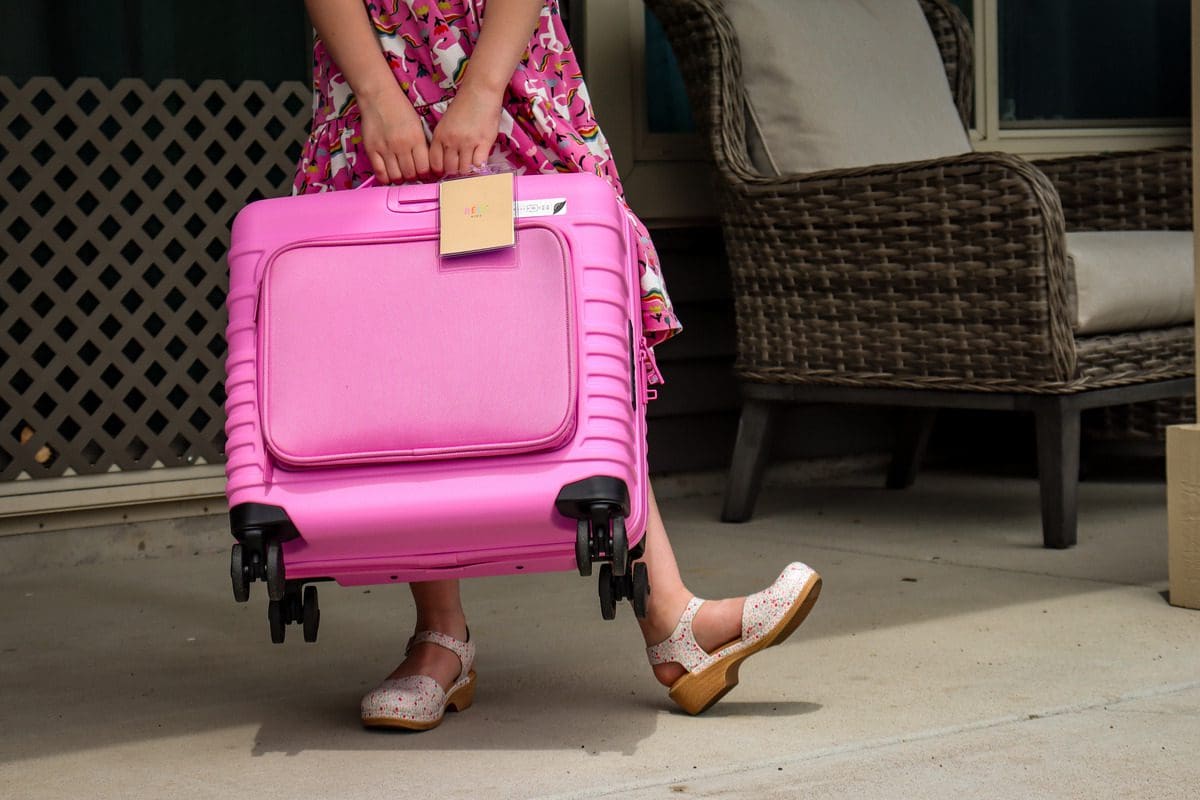 A close up of a young girl holding her pink luggage.