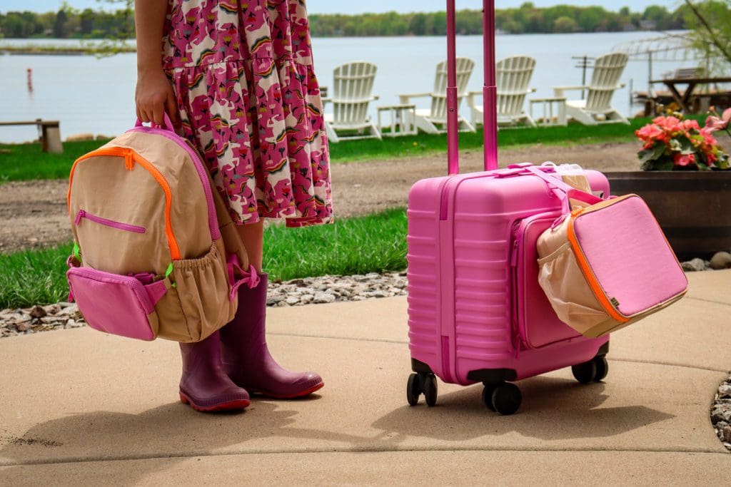 A young girl stands with her BÉIS Kids Roller, backpack, and lunch box.