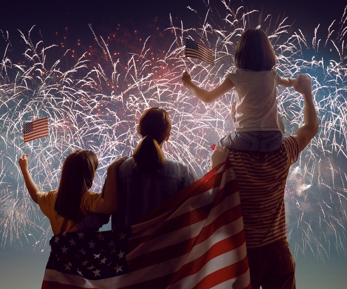 A family with American flags watching the Fourth of July fireworks.