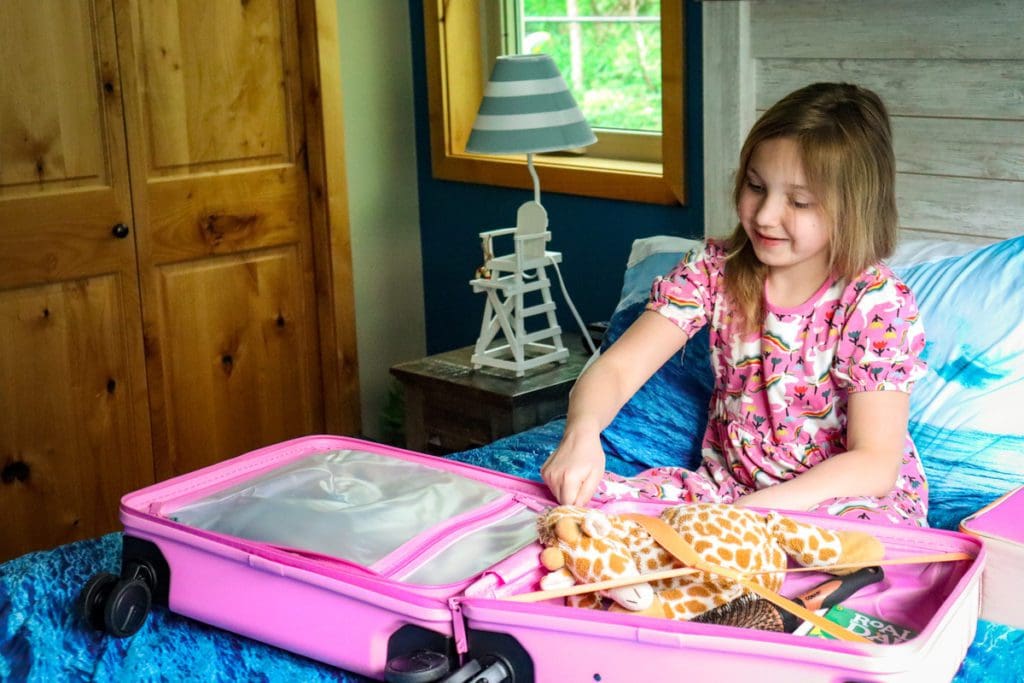 A child packing her belongings in a pink suitcase.