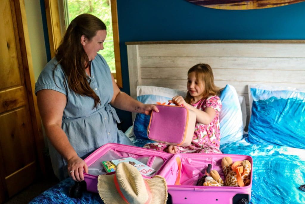 A mom and her young daughter pack a suitcase together.